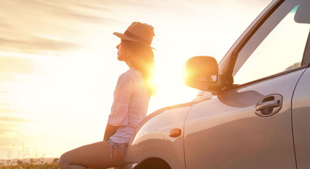 Woman sitting on hood of car during sunset
