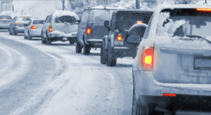 A line of cars on a snowy road following safety tips for driving in snow and ice