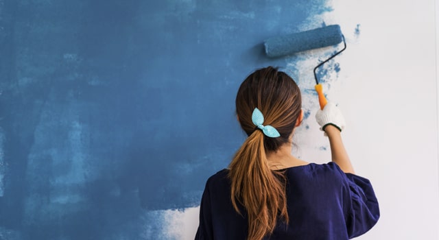 Woman painting white wall blue with roller
