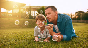 father and son lying on lawn blowing bubbles