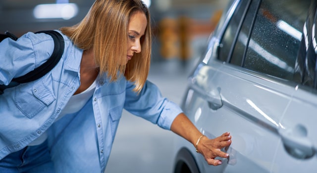 woman touching dent on parked car