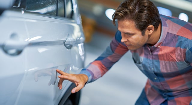 Man looking at damage from someone who hit his parked car