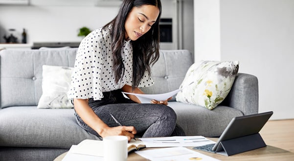 Young woman sitting on sofa writing notes in front of laptop