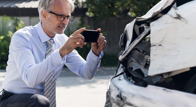 Man taking photo of totaled car for insurance pay