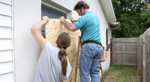 two men placing plywood over a window preparing for a hurricane