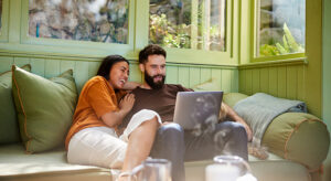 Young couple sitting on a sofa reviewing their insurance on their laptop
