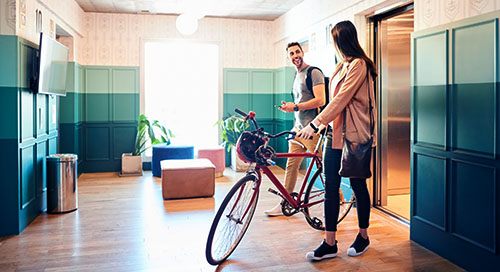 A young man talking to a young woman with her bike in a condo lobby