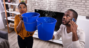 Young couple holding buckets under leaky ceiling while calling insurance company