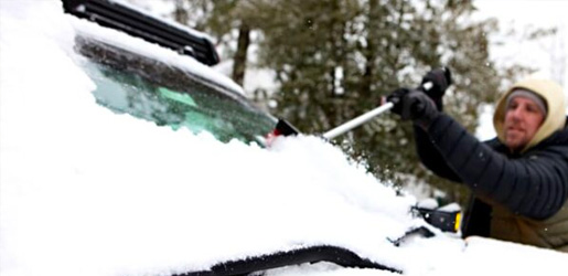 Man clearing snow off of windshield with brush