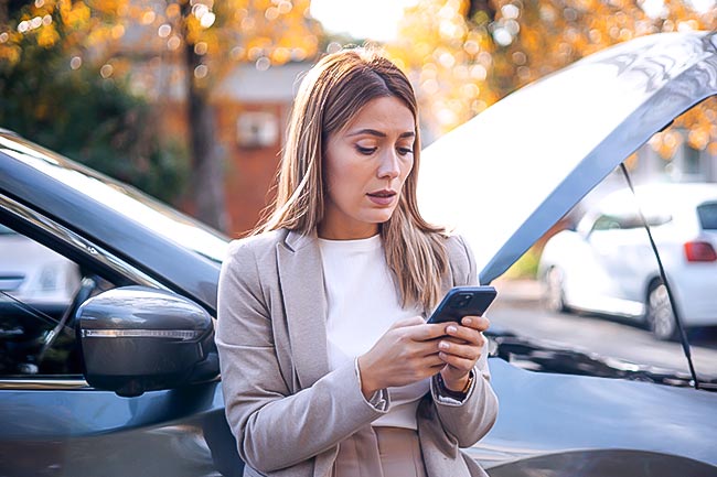 woman on her phone with broken down car behind her