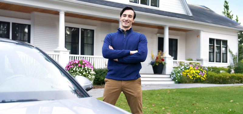 Confident man with his insurance standing in front of a home next to a car