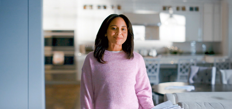 woman in pink sweater standing and smiling near kitchen.
