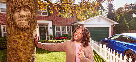 Photo of a woman leaning on and looking up at a tree. The tree has a face on it.