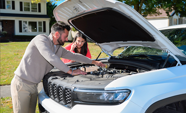 Dad working on car with hood up with daughter on cell phone