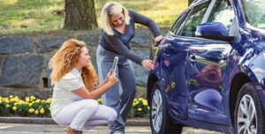 Mom and daughter viewing dent in blue car