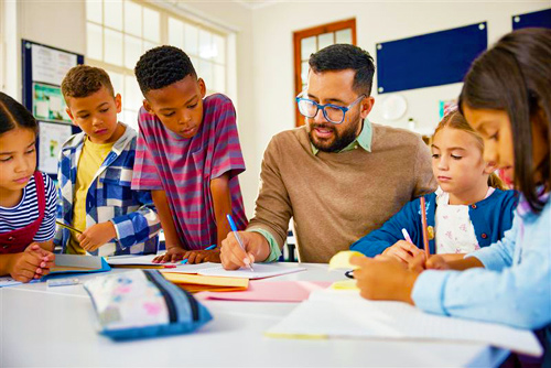 Photo of a teacher writing at a table surrounded by students