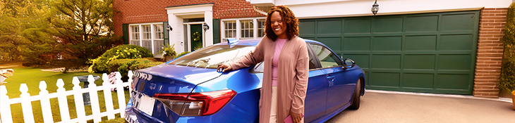 Woman smiling leaning up against a blue car in her driveway with home in background