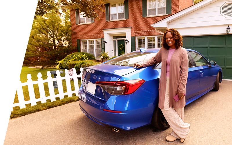 Woman smiling leaning up against a blue car in her driveway with home in background