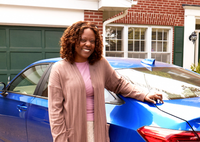 Photo of a woman leaning on a car standing in front of a house