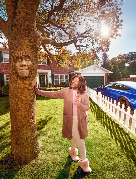 Photo of a woman leaning on and looking up at a tree. The tree has a face on it.