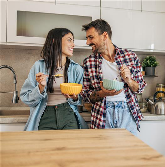 Young couple eating breakfast in kitchen leaning up against counter