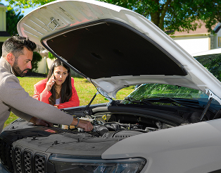 Father showing daughter parts of car engine with hood up