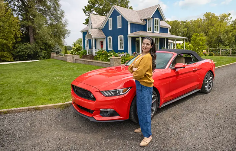 Woman standing in front of red ford mustang with home in the background